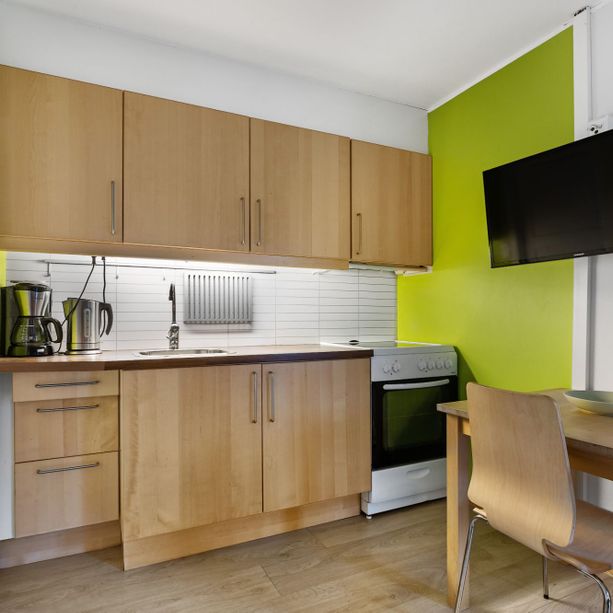 Moderne kjøkken med hvitevarer og spisebord og stoler samt en tv på veggen